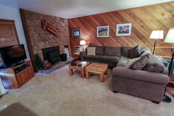 A cozy living room with a stone fireplace, wooden walls, a large brown sofa, two wooden coffee tables, and a television on a wooden stand. - Snowcreek I 39 Pet-Friendly, Private Washer Dryer, Mountain Views by RedAwning (Mammoth Lakes)