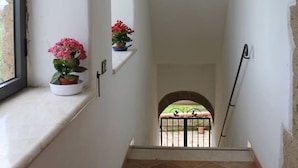 Ein schmaler Flur mit einem Fenster links, einem gefliesten Boden und Blick auf einen Innenhof am Ende.