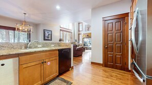 Enjoy cooking in the well-equipped kitchen with a granite countertop, stainless steel appliances, and wooden cabinetry, leading to a cozy living area with a fireplace and outdoor views.