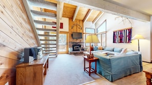 A cozy living room with a fireplace, a sofa, a TV, and a wooden staircase. - Wildflower 6 Spacious, Rustic, Walk to Shop and Restaurants by RedAwning (Mammoth Lakes)