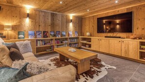 A cozy living room with a wooden ceiling, a large flat-screen TV, bookshelves, a sofa, and a coffee table. - Chalet Birdie + Mazot: elegant and spacious property in Les Houches (Les Houches)