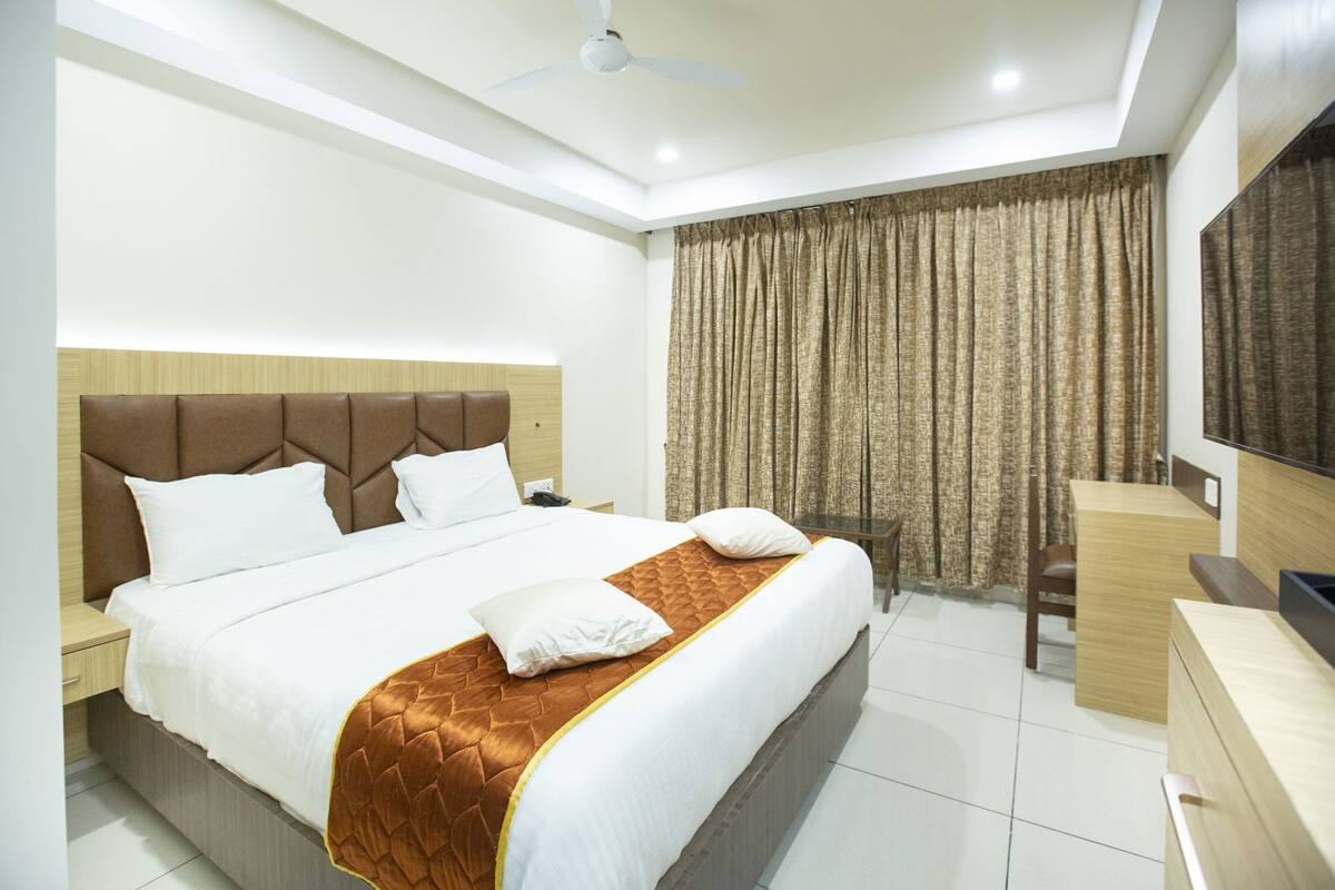 A hotel room with a large bed, a desk, a chair, a TV, and a ceiling fan.