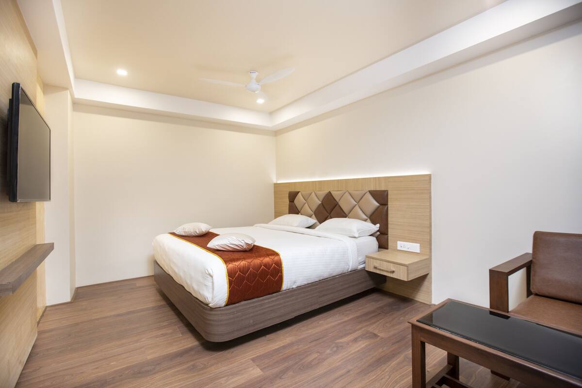 A modern hotel room with a bed, a nightstand, a chair, and a flat-screen TV mounted on the wall.