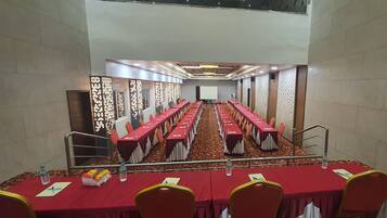 A conference room with long tables, chairs, and a projector screen at the front.