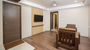 A modern room with a wooden door, a flat-screen TV mounted on the wall, a ceiling fan, and a wooden chair. - Hotel Ark (Kumbakonam)