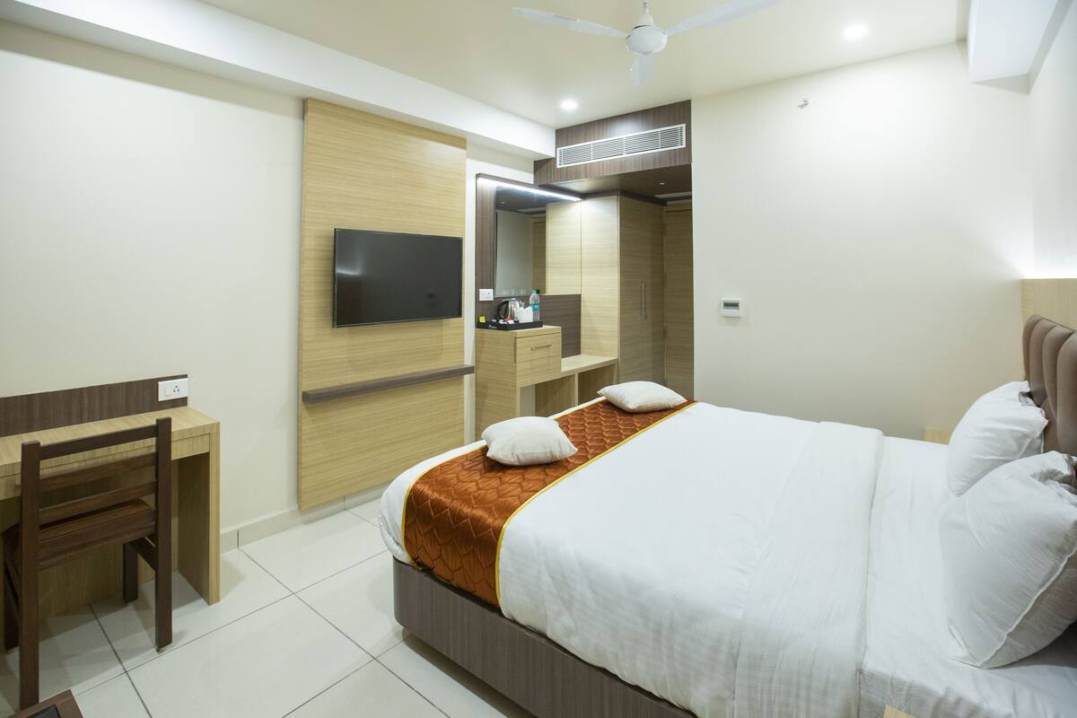 A hotel room with a bed, a desk, a chair, a TV, and a wardrobe.