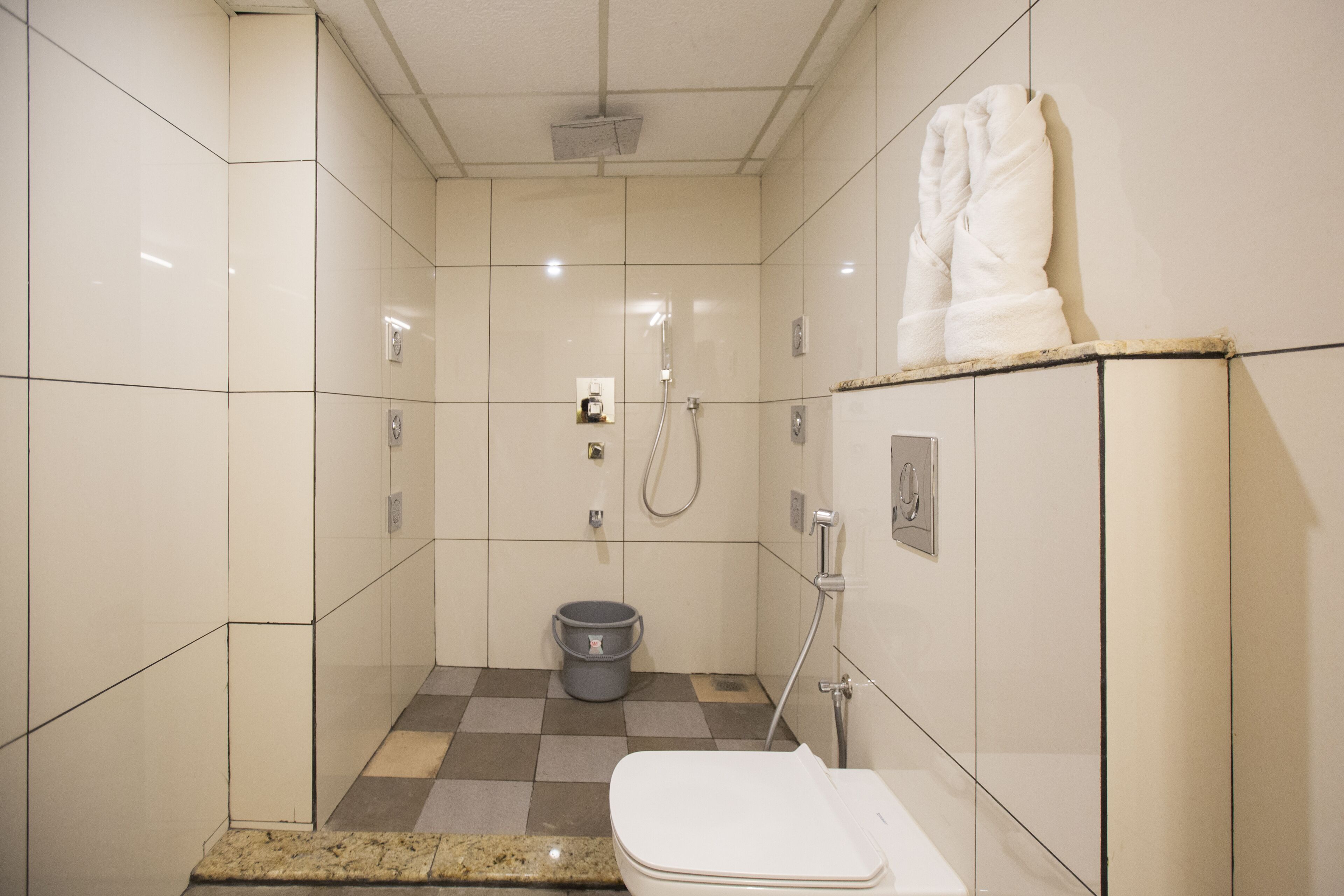 A small, tiled bathroom with a toilet, a shower, and a bucket.