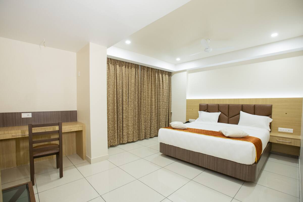 A hotel room with a bed, desk, chair, and curtains.