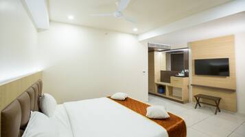 A hotel room with a bed, a ceiling fan, a TV mounted on the wall, and a small wooden bench.