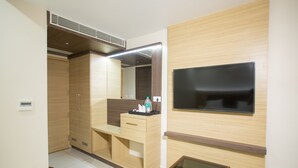 A modern hotel room with a wooden wardrobe, a small desk with a mirror, a flat-screen TV mounted on the wall, and a small table. - Hotel Ark (Kumbakonam)
