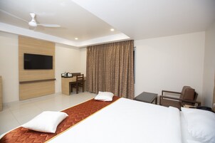 Una habitación de hotel con cama, escritorio, silla, televisor y ventilador de techo.