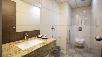 A modern bathroom with a granite countertop sink, a mirror, a shower, and a toilet.