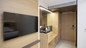 A modern hotel room with a flat-screen TV, a wooden vanity with a mirror, a sink, and a small countertop with toiletries.