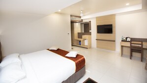 A modern hotel room with a large bed, a desk, a TV, and a bathroom area. - Hotel Ark (Kumbakonam)