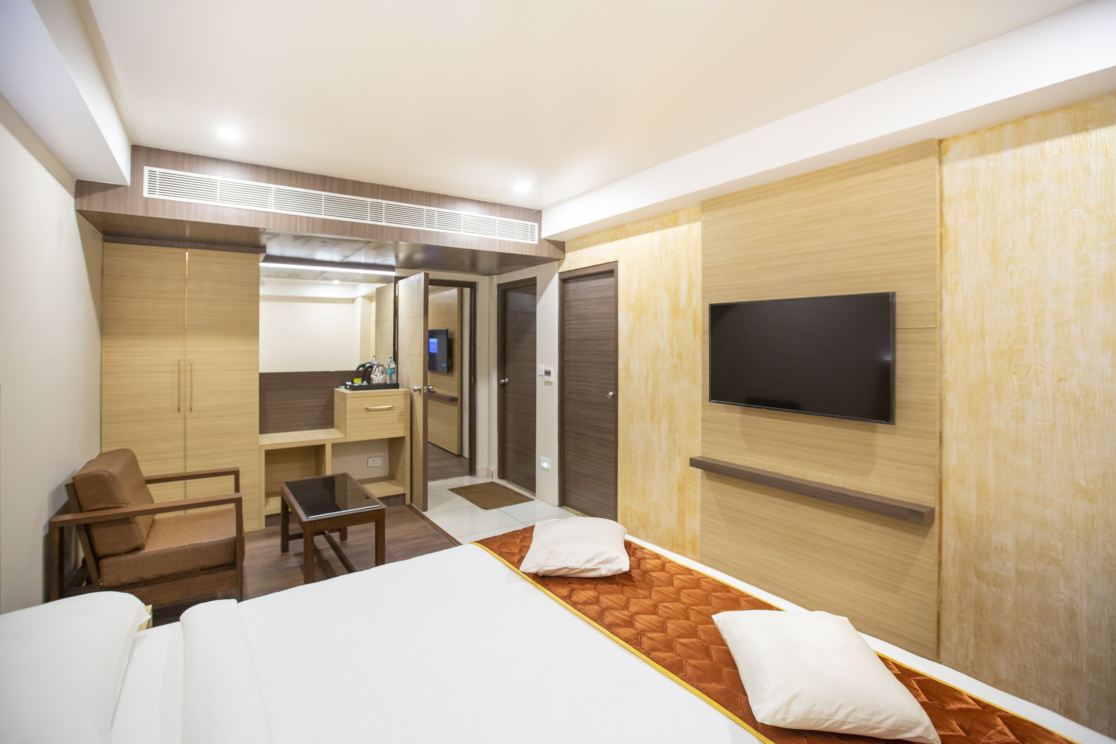 Quarto de hotel com cama, escrivaninha, cadeira, televisão e guarda-roupa.
