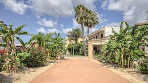 Un chemin menant à un bâtiment doté d’un balcon, entouré de bananiers et de palmiers.