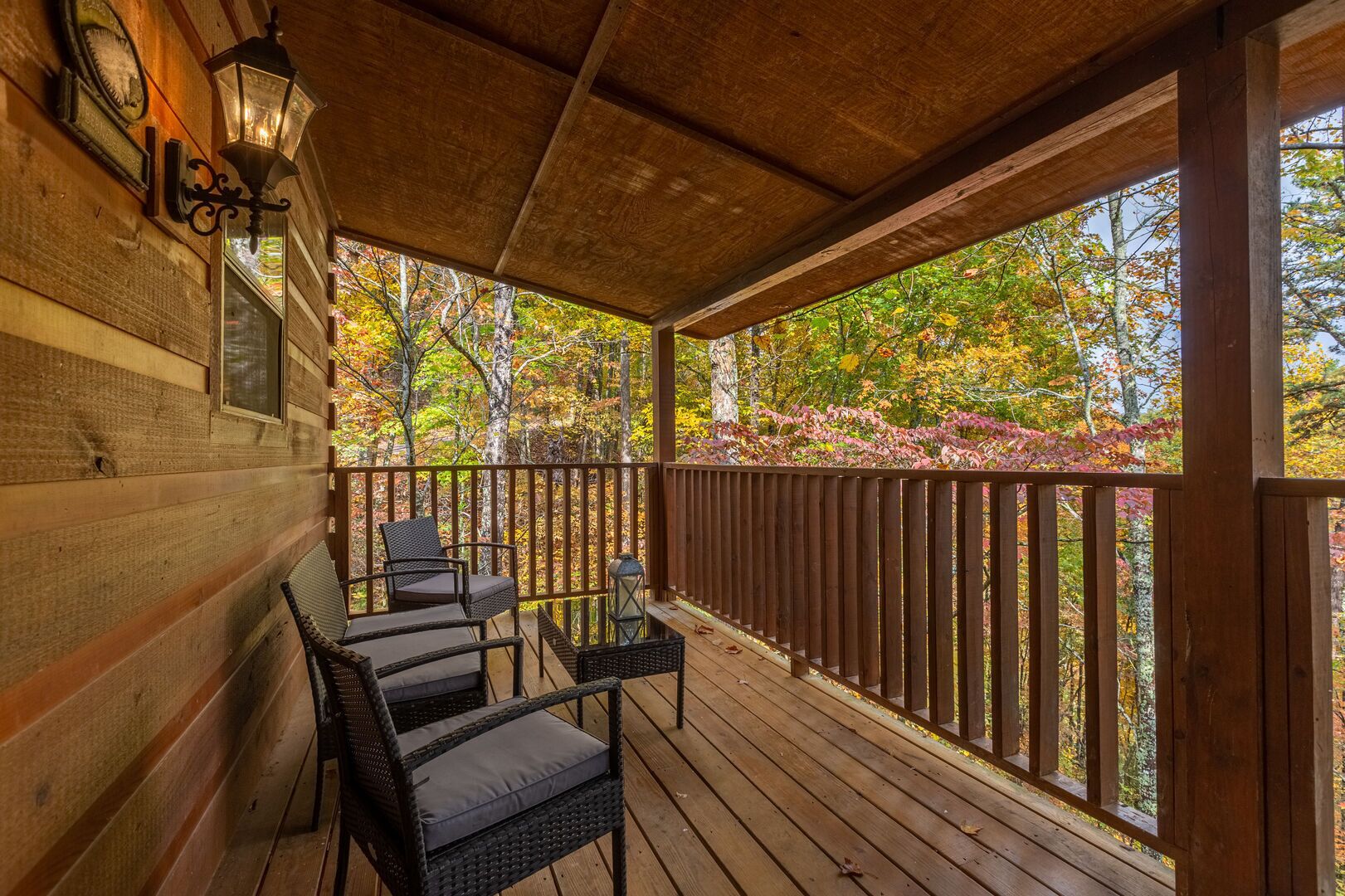 A wooden deck with a railing, wicker chairs, and a table.