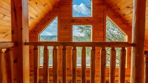 A wooden cabin with a balcony and large windows offering a view of trees and mountains.