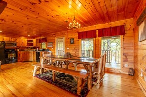 A rustic cabin interior with a wooden dining table, kitchen area, and large windows. - Amazing Mountain View Cabin with Jacuzzis, Hot Tub & StarlinkWIFI! Pets Welcome! (Sevierville)