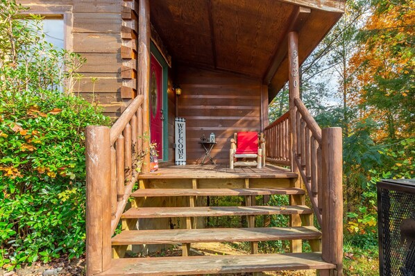 A wooden cabin with a porch, a welcome sign, a chair, and a table. - Amazing Mountain View Cabin with Jacuzzis, Hot Tub & StarlinkWIFI! Pets Welcome! (Sevierville)