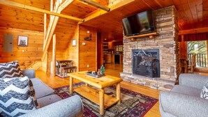 A cozy log cabin interior with a stone fireplace, wooden furniture, and a television mounted above it.