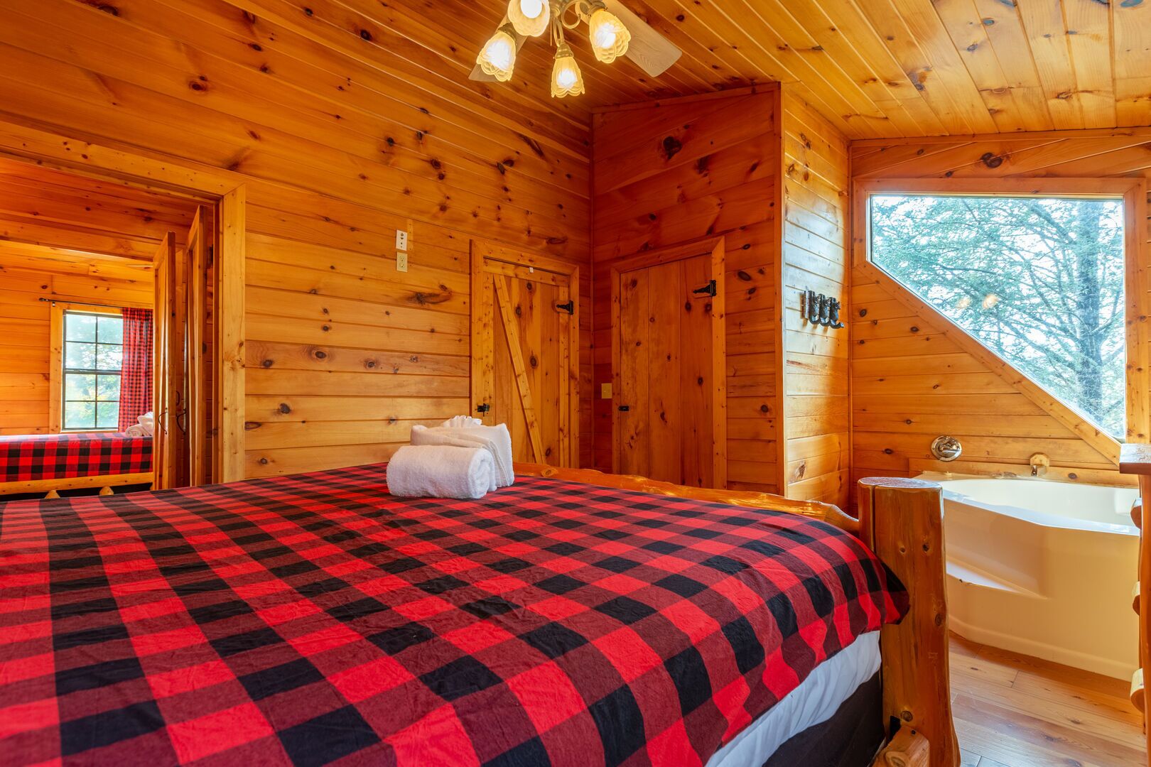 Een knus kamer in een blokhut met een geruit beddegoed, houten plafond en een groot raam.