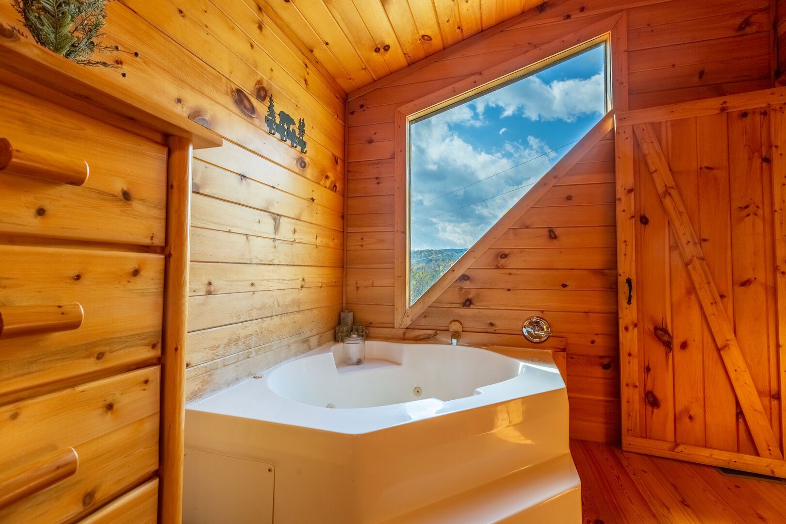 A wooden cabin interior with a large bathtub, wooden walls, and a window offering a view of the sky.
