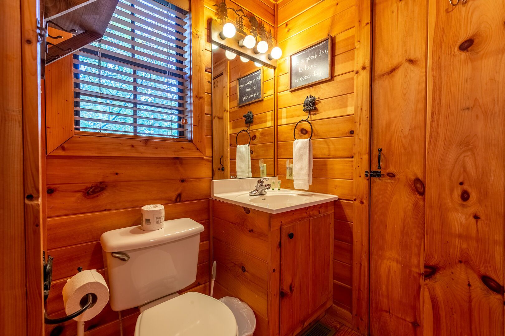 Un baño de cabaña de madera con inodoro, lavamanos y ventana.