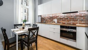 Una cocina compacta con armarios blancos, salpicadero de ladrillo y comedor con mesa dispuesta para cuatro.