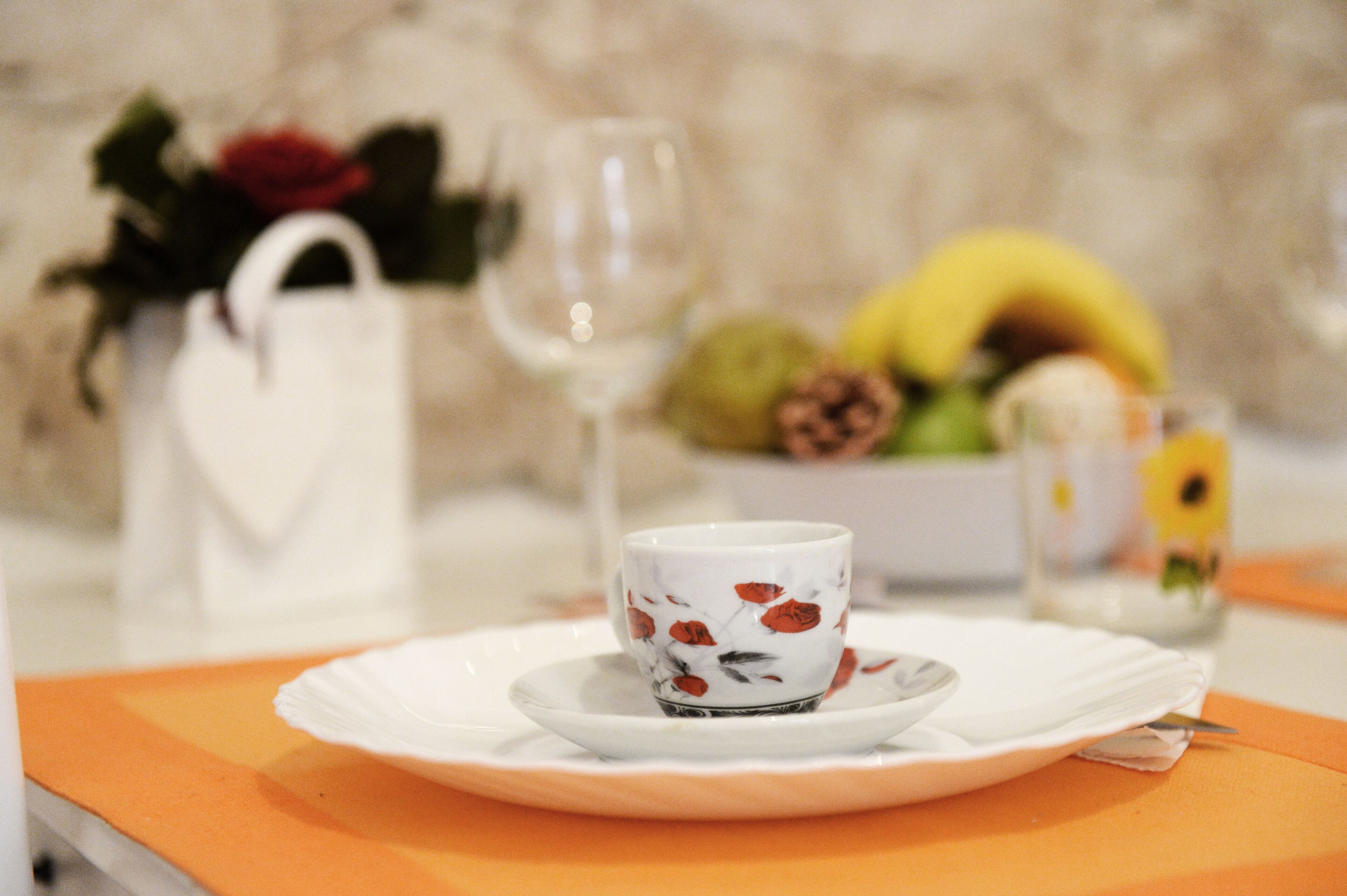 Una mesa de comedor con un plato blanco, una taza con flores y un vaso de agua.