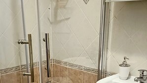 Et badeværelse med brusekabine i glas, en hvid vask og et toilet.