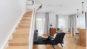 Een moderne woonkamer met een houten trap, een eethoek en een keuken.