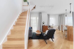 A modern living room with a wooden staircase, a dining area, and a kitchen.