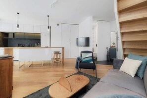 A modern living space with a kitchen, a sofa, a TV, and a staircase.