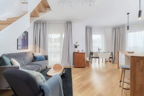 A modern living room with a sofa, a dining area, and a staircase.