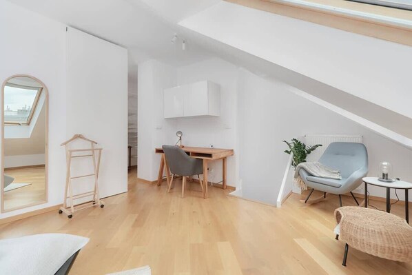 A modern loft bedroom with a skylight, a desk, a chair, and a small side table.