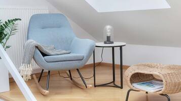 A room with a blue chair, a small round table with a light bulb, a wicker chair, and a white radiator.
