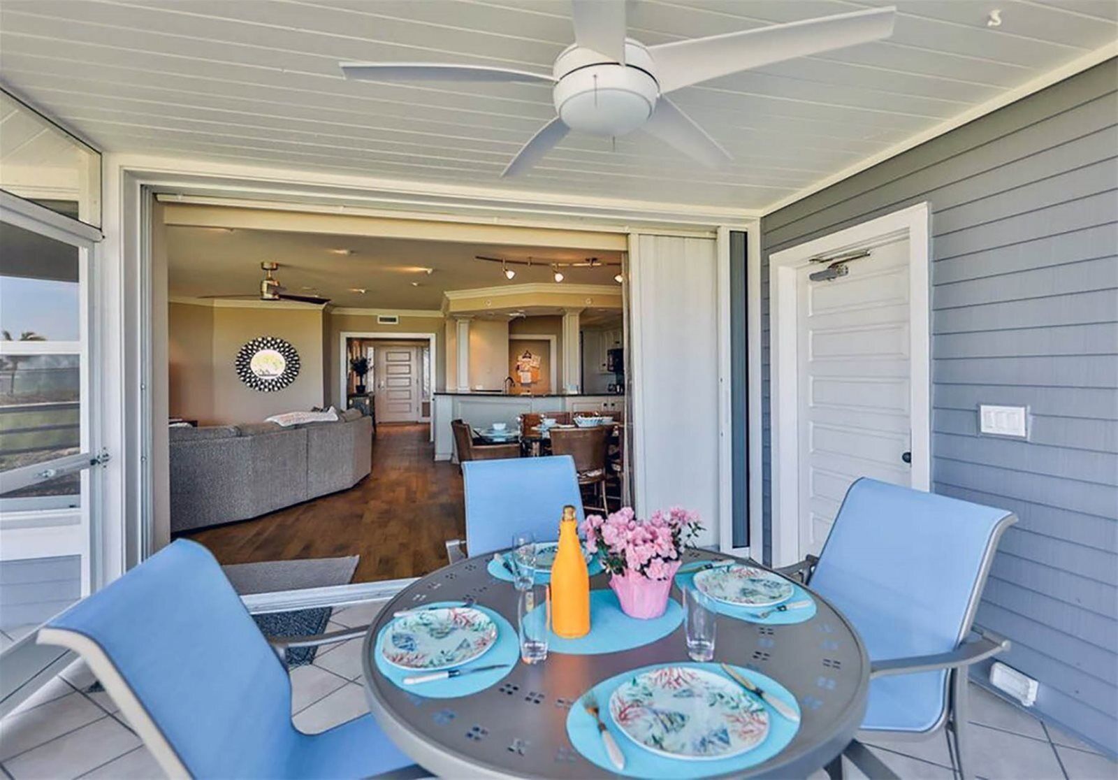 An open patio with a round table set for dining, surrounded by chairs, and a ceiling fan above.