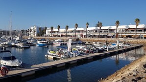 A marina with various boats docked, a stone breakwater, and a building with palm trees in the background. - Spacious Marina Apartment lovely balcony view, near to pool, WiFi & UK Tv (Lagos)