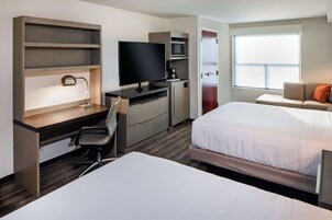Ein Hotelzimmer mit einem Bett, einem Schreibtisch mit Computer, einem Fernseher, einer Mikrowelle und einem Fenster mit Blick.