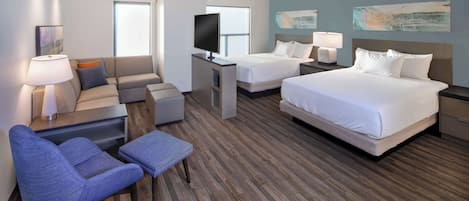 A hotel room with two beds, a TV, a sofa, and a desk.