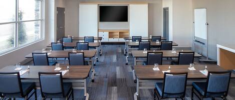 A conference room with multiple tables and chairs, a large flat-screen TV, and a whiteboard.