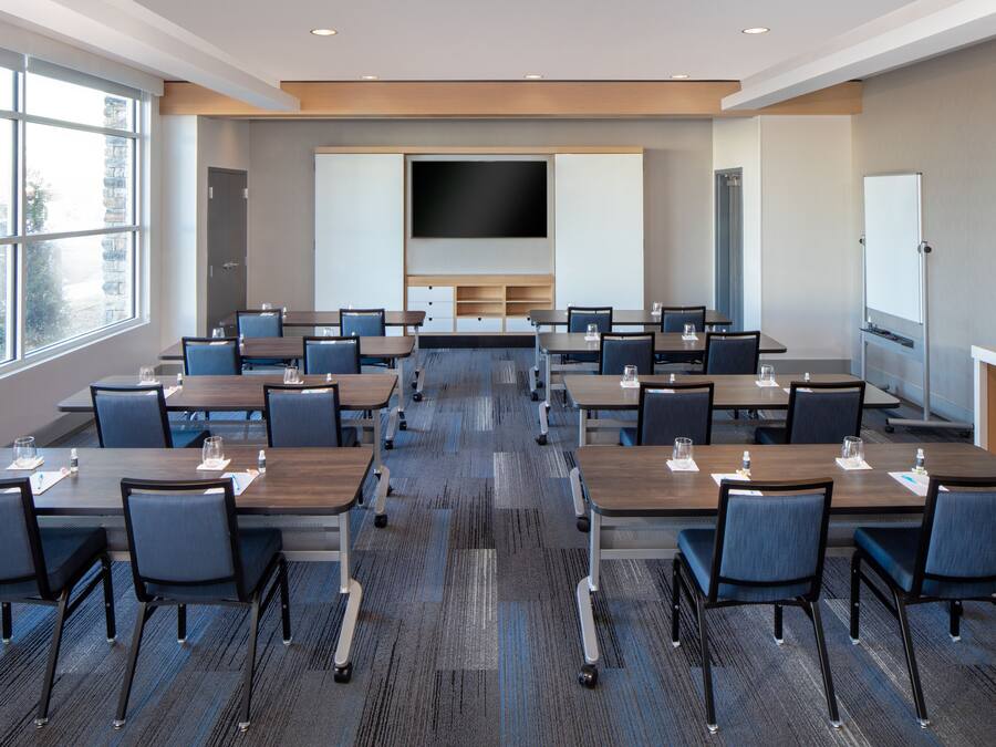 A conference room with multiple tables and chairs, a large flat-screen TV, and a whiteboard.