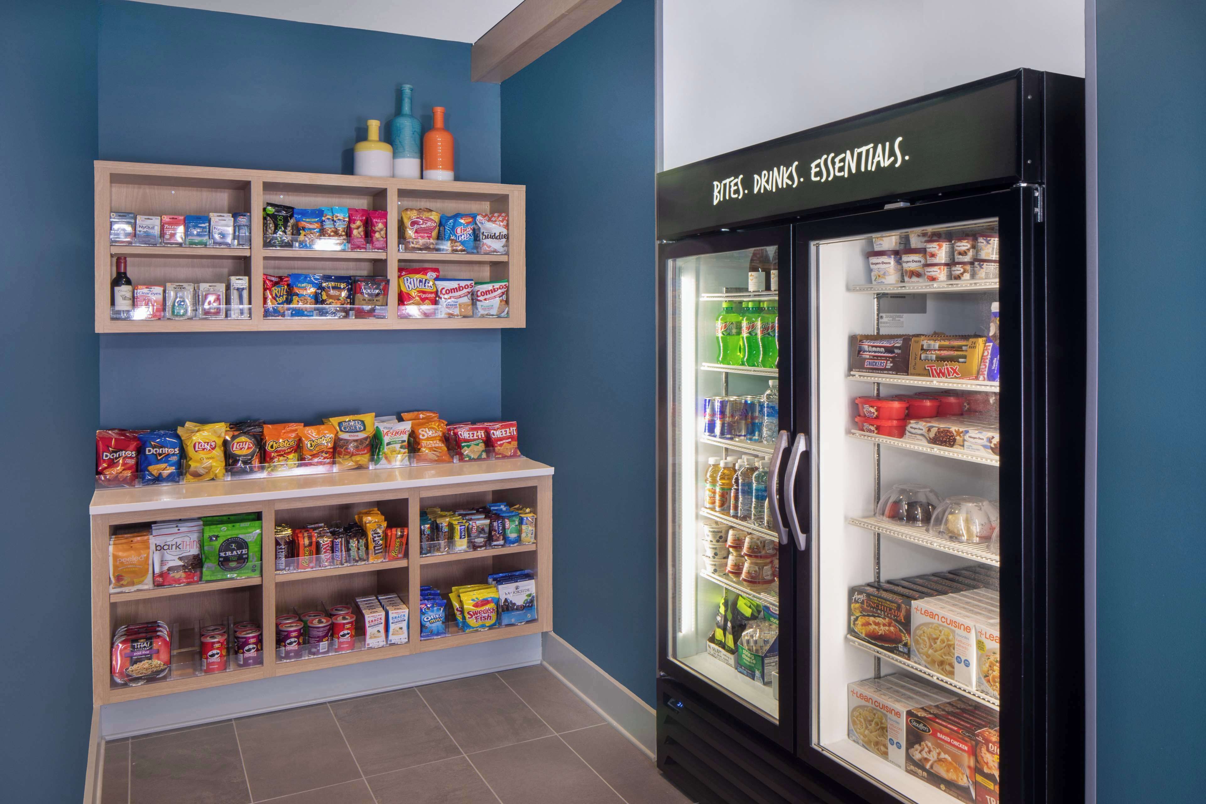 Un espace de vente automatique proposant des collations et des boissons, avec divers produits emballés et un rayon réfrigéré intitulé « Encas, boissons, produits de première nécessité ».