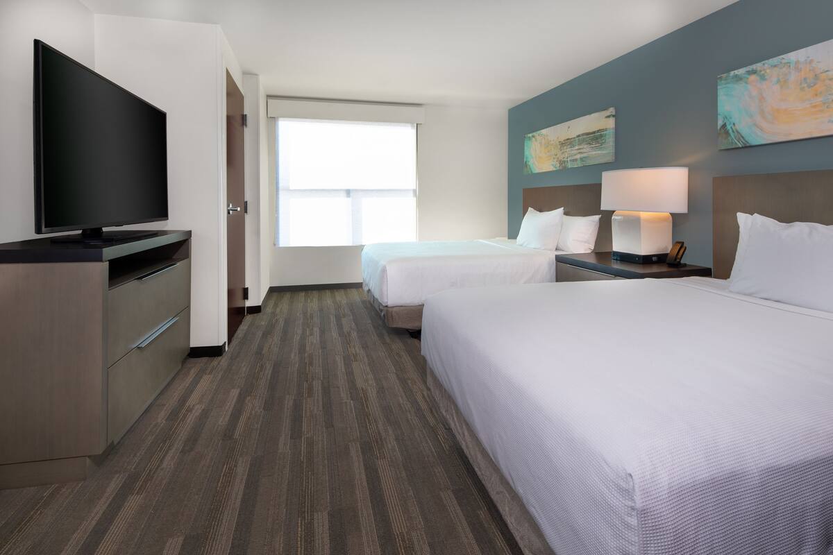 A hotel room with two beds, a TV, a desk, and a window.