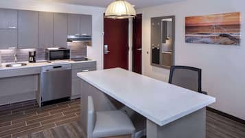 Una cocina moderna con gabinetes grises, un microondas, una cafetera y un lavabo. Hay un banco de madera en la isla de la cocina.