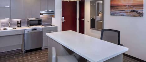 A modern kitchen with grey cabinets, a microwave, a coffee maker, and a sink. There's a wooden bench at the kitchen island.