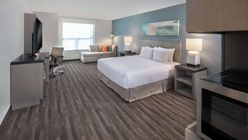 A modern hotel room with a large bed, a desk with a flat-screen TV, a sofa, and a dining table.