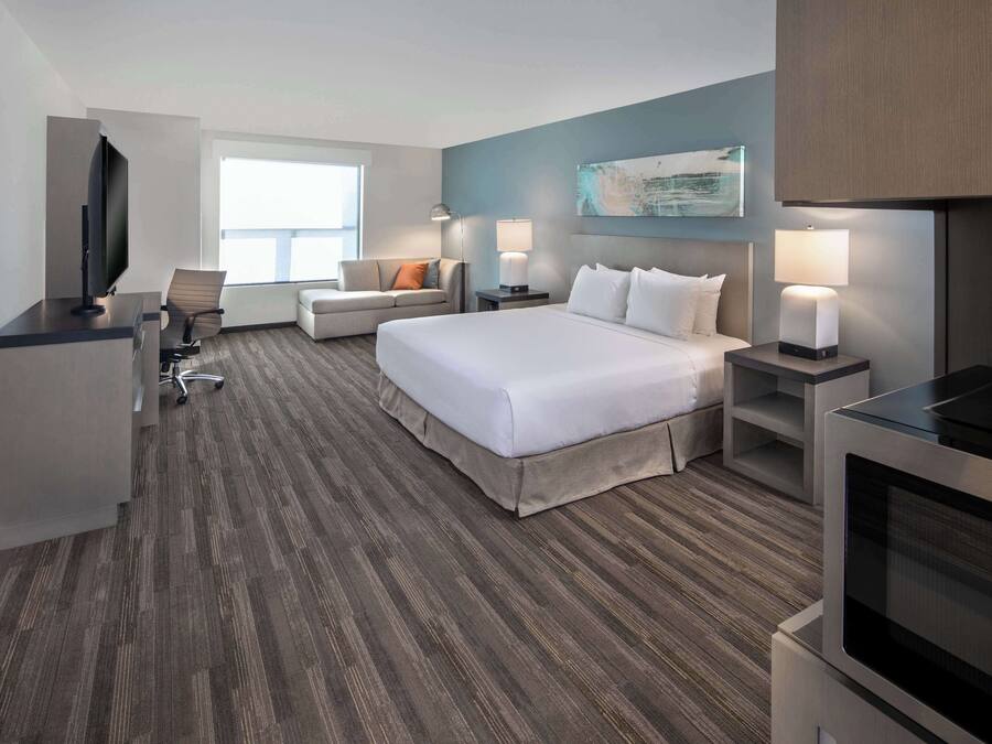 A modern hotel room with a large bed, a desk with a flat-screen TV, a sofa, and a dining table.