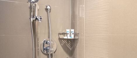 Ein Duschbereich mit Handbrause, Wandarmatur und Duschschlauch. Eine kleine Ablagefläche mit Toilettenartikeln ist vorhanden.